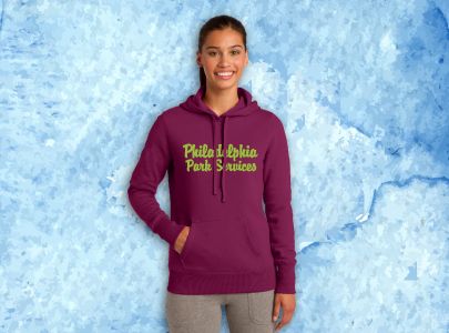 Woman wearing burgundy, hooded sweatshirt screen printed with Philadelphia Park Services with hand in front pocket looking warm
